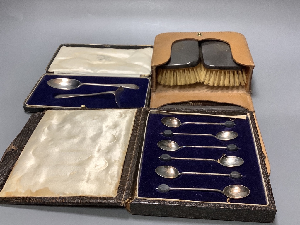 A cased pair of silver mounted clothes brushes, a cased silver spoon and pusher and a cased set a silver bean end coffee spoons.